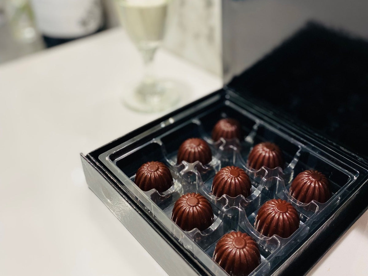 An open box of nine Xoxoa bonbons beside a glass of sparkling wine